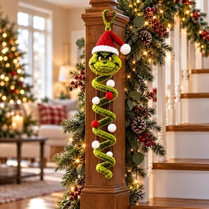 Peut inclure: Une décoration en spirale crochetée verte représentant une tête de personnage avec un bonnet de Père Noël rouge et blanc. Le corps en spirale est orné de petits pompons crochetés blancs et rouges fixés par des fils, suspendu par une boucle.