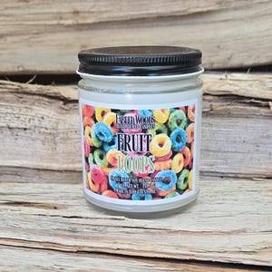 Puede incluir: Una vela en tarro de vidrio con tapa negra y una etiqueta con cereales coloridos. La etiqueta dice "FRUIT LOOPS" y "FABLED WOODS HANDPOURED CANDLES". La vela pesa 198,4 g netos y está hecha en Ashe County, NC.