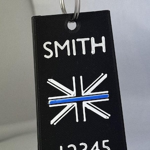 May include: Black rectangular keyring with the name "SMITH", a white and blue UK flag design, and the number "12345" in white. The keyring is attached to a silver ring.