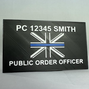 May include: Black and white 3D printed plaque with a blue line and the text "PC 12345 SMITH PUBLIC ORDER OFFICER".