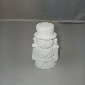 May include: White ceramic nutcracker figurine with a painted face and a tall hat. The figurine is ready to be painted.
