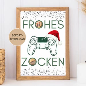 May include: A framed print with a festive design. The print features the German words "Frohes Zocken" in green, meaning "Happy Gaming", with a controller wearing a Santa hat. The number "50" is incorporated into the word "Frohes". A small circle on the left says "SOFORT-DOWNLOAD".