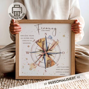 May include: A framed print with a compass rose design, featuring text in German. The artwork includes a watercolor-style compass with blue, yellow, and brown hues. The frame is made of light-coloured wood, and the print is labelled "DIGITALE DATEI" and "PERSONALISIERT".
