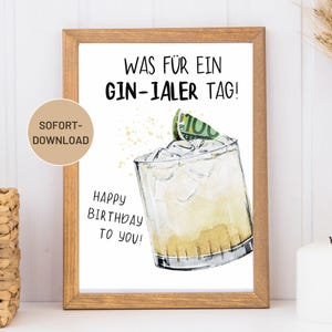 May include: A framed print with the text "WAS FÜR EIN GIN-IALER TAG!" and "HAPPY BIRTHDAY TO YOU!" features a watercolor illustration of a cocktail with ice and a lime wedge. The print is in a wooden frame.