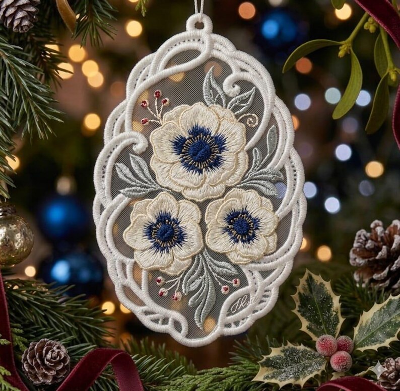 May include: An oval-shaped white lace ornament featuring an intricate embroidered design of three cream-colored flowers with dark blue centers, surrounded by light green leaves and small red berries, all set against a sheer mesh fabric background.
