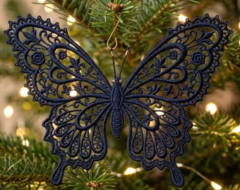 May include: A dark navy blue butterfly ornament crafted from intricate lace embroidery. The design features detailed filigree patterns throughout the wings and body, with a small gold-toned metal hook attached to the top for hanging purposes.