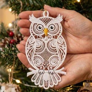 May include: A white lace owl ornament featuring intricate embroidery patterns, large black and white eyes, and a yellow beak. The owl is perched on a branch and includes a small loop at the top for hanging, showcasing detailed thread work.