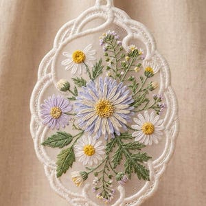 May include: An oval-shaped white lace ornament featuring intricate machine embroidery of a floral bouquet. The design includes light purple and white daisies with yellow centers, green leaves, and small lavender buds on a sheer mesh fabric background.