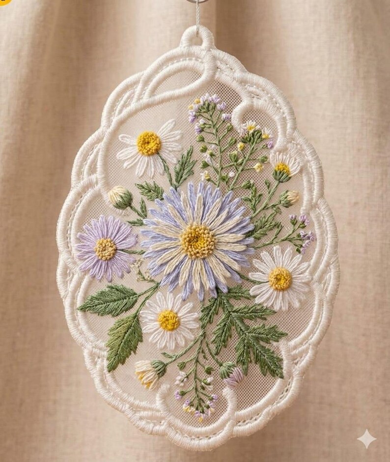 May include: An oval-shaped white lace ornament featuring intricate machine embroidery of a floral bouquet. The design includes light purple and white daisies with yellow centers, green leaves, and small lavender buds on a sheer mesh fabric background.