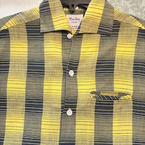 May include: A short-sleeve button-down shirt featuring a yellow and dark gray plaid pattern with thin horizontal lines. The shirt has a pointed collar, a single chest pocket, and white buttons. A label inside the collar reads Mark Twain.