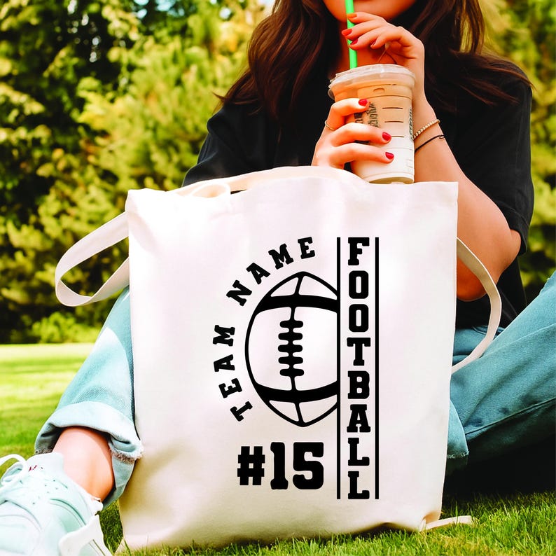 May include: Cream-colored tote bag with a black football graphic, the words "TEAM NAME" in a semi-circle, and "FOOTBALL" vertically. The number "15" is below the football. The bag has long handles.