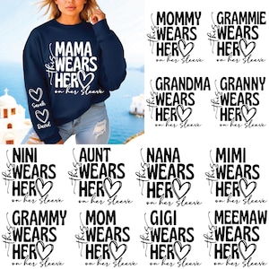 May include: Navy blue sweatshirt with the text "MAMA WEARS HER" and a heart design. The sleeve features the names "Sarah" and "David" inside hearts. Additional designs include "MOMMY WEARS HER" and "GRAMMIE WEARS HER".