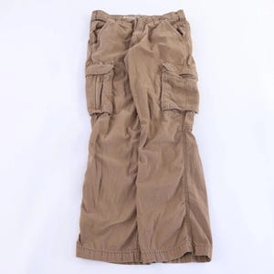 May include: A pair of tan cargo pants featuring a button and zipper fly closure, two side slash pockets, and two large rectangular cargo pockets on the thighs with flap closures. The pants have a straight-leg cut and a standard waistband with belt loops.