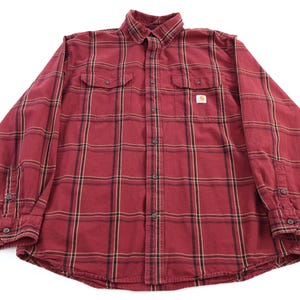 Könnte beinhalten: Ein rot-schwarz kariertes Button-Down-Hemd mit langen Ärmeln. Das Hemd hat zwei Brusttaschen und einen kleinen Carhartt-Logoaufnäher. Das Karomuster enthält dünne gelbe Streifen. Das Hemd ist aus robustem Stoff gefertigt.