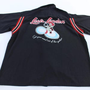 Puede incluir: Camiseta negra de manga corta con un gráfico temático de bolos en la espalda. El gráfico presenta un personaje de dibujos animados en un bollo de bolos con el texto "Louis London" y "Get your mind out of the gutter."