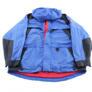 May include: Blue and black hooded jacket with a red zipper and red lining. The jacket has black panels on the shoulders and sleeves. A practical and stylish outerwear piece.