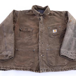 May include: Brown work jacket with four front pockets, a button-up closure, and a collared neckline. The jacket features the Carhartt logo on one of the pockets. The jacket is made of a durable, worn material.