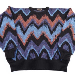 Könnte beinhalten: Ein langärmeliger Strickpullover mit einem markanten Zickzackmuster in Schwarz, Blau und Kupfer. Das Kleidungsstück hat einen Rundhalsausschnitt, gerippte Bündchen und einen gerippten Saum. Ein kleines rechteckiges Etikett mit "BARRONS CODD" ist am Kragen.