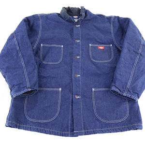 May include: A blue denim work jacket with a quilted lining. The jacket has a button-up front, four front pockets, and a small red logo patch. The collar is a darker blue. The jacket is a medium weight.