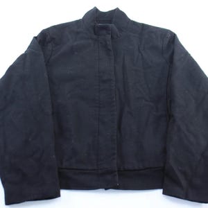 Puede incluir: Una taza de cerámica blanca con un asa negra y el texto "But First, Coffee" en negrita negra. La taza se encuentra sobre un fondo neutro, resaltando su diseño simple.