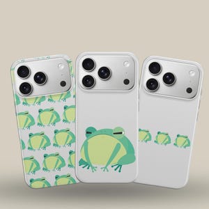 May include: Three white phone cases with green and yellow frog designs. One case has a repeating pattern of frogs, another features a single frog, and the third has three frogs. The cases have a glossy finish and a camera bump.