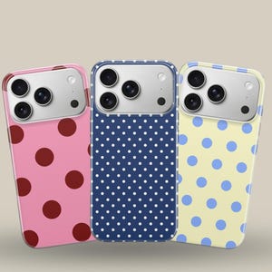 Può includere: Tre custodie per telefono con motivi a pois. Una è rosa con pois rosso scuro, un'altra blu navy con pois bianchi e la terza gialla con pois azzurri. Le custodie hanno un modulo fotocamera argentato.