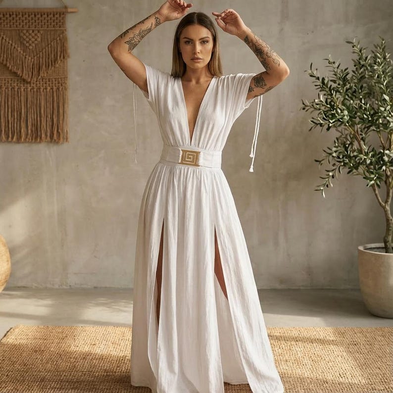 May include: A white maxi dress with a plunging neckline and short sleeves. The dress features a gold-colored belt with a square buckle and high slits on the front. The dress has a flowing, elegant design, suitable for a special occasion.