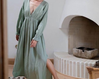 May include: A long, sage green dress with a deep V-neck and long sleeves. The dress features a gathered waist and a high side slit. The sleeves have ruffled cuffs. The dress is made of a lightweight fabric, suitable for warm weather.