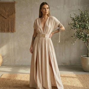 May include: A beige maxi dress with a plunging neckline and short sleeves. The dress features a high waist with a decorative belt and two high slits in the front. The dress is made of a lightweight fabric.