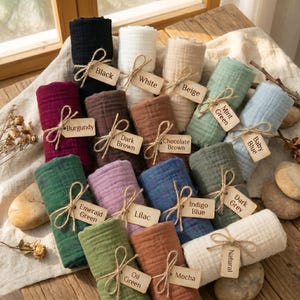 Puede incluir: Una colecci&oacute;n de rollos de tela en varios colores, incluyendo negro, blanco, beige y burdeos. Cada rollo est&aacute; atado con hilo y etiquetado con un nombre de color. El surtido incluye tonos de verde, azul, marr&oacute;n y morado.