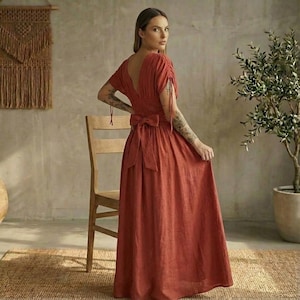 May include: A rust-colored maxi dress with a deep V-neck and short sleeves. The dress features a bow at the waist and a flowing skirt. The dress is made of a lightweight fabric, perfect for warm weather.