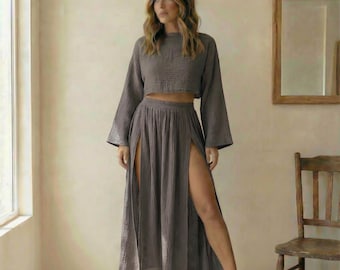 May include: A two-piece set in a muted gray color. The top is a long-sleeved crop top, and the skirt has high slits on both sides. The fabric appears to be a lightweight, textured material. The outfit is worn by a person.