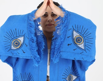 May include: A blue linen kimono with fringe detailing and embroidered evil eye designs. The kimono is open in the front and has a relaxed fit.