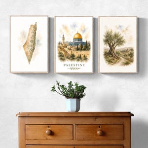 Può includere: Un set di tre stampe da parete incorniciate. La stampa a sinistra mostra una mappa della Palestina con motivi floreali. Quella centrale raffigura la Cupola della Roccia con il testo PALESTINE. Quella a destra mostra un ulivo in un paesaggio.