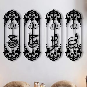 Op de afbeelding: Vier zwarte metalen wanddecoraties met ingewikkelde ontwerpen en Arabische kalligrafie. De stukken zijn in een rij op een witte muur geplaatst.