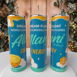 May include: Three teal Alani Nu Energy drink tumblers with silver straws. The tumblers have a yellow and orange top, with the words "DREAM FLOAT" and "Alani Nu ENERGY" printed on them. A smiling lemon graphic is also visible.