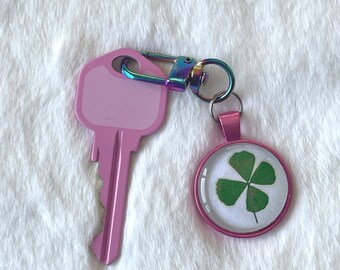 May include: A pink key with a four-leaf clover charm attached to a rainbow-colored metal key chain.