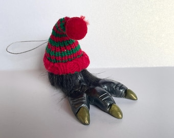 May include: A black and gold claw ornament with a red and green striped knit hat. The ornament is a Christmas decoration.