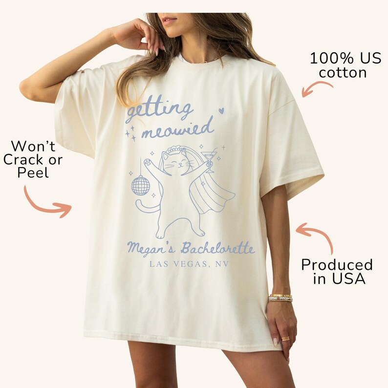 May include: Cream-colored oversized t-shirt with the phrase "getting meowied" and a cartoon cat in a veil, holding a disco ball and a cocktail. The text "Megan's Bachelorette Las Vegas, NV" is below the cat. Made of 100% US cotton.