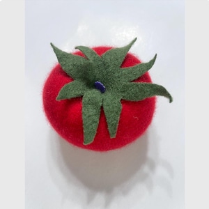 Könnte beinhalten: Eine handgefertigte Tomate aus Filz mit einem grünen Blattoberteil und einem kleinen lila Akzent. Die Tomate ist leuchtend rot, und die Blätter sind tiefgrün. Dieser Dekorationsartikel ist wahrscheinlich ein Bastel- oder Einrichtungsgegenstand.