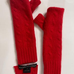 May include: A pair of bright red fingerless gloves with a cable knit design. The gloves are made of a soft material and have a small label attached. The label reads "RALPH LAUREN" and "S MADE IN CHINA".