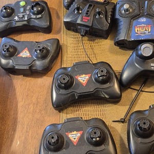 Pu&ograve; includere: Una collezione di telecomandi neri, alcuni con il logo "Monster Jam". I telecomandi hanno vari layout di pulsanti e design, alcuni con antenne e altri con il logo "Heat".