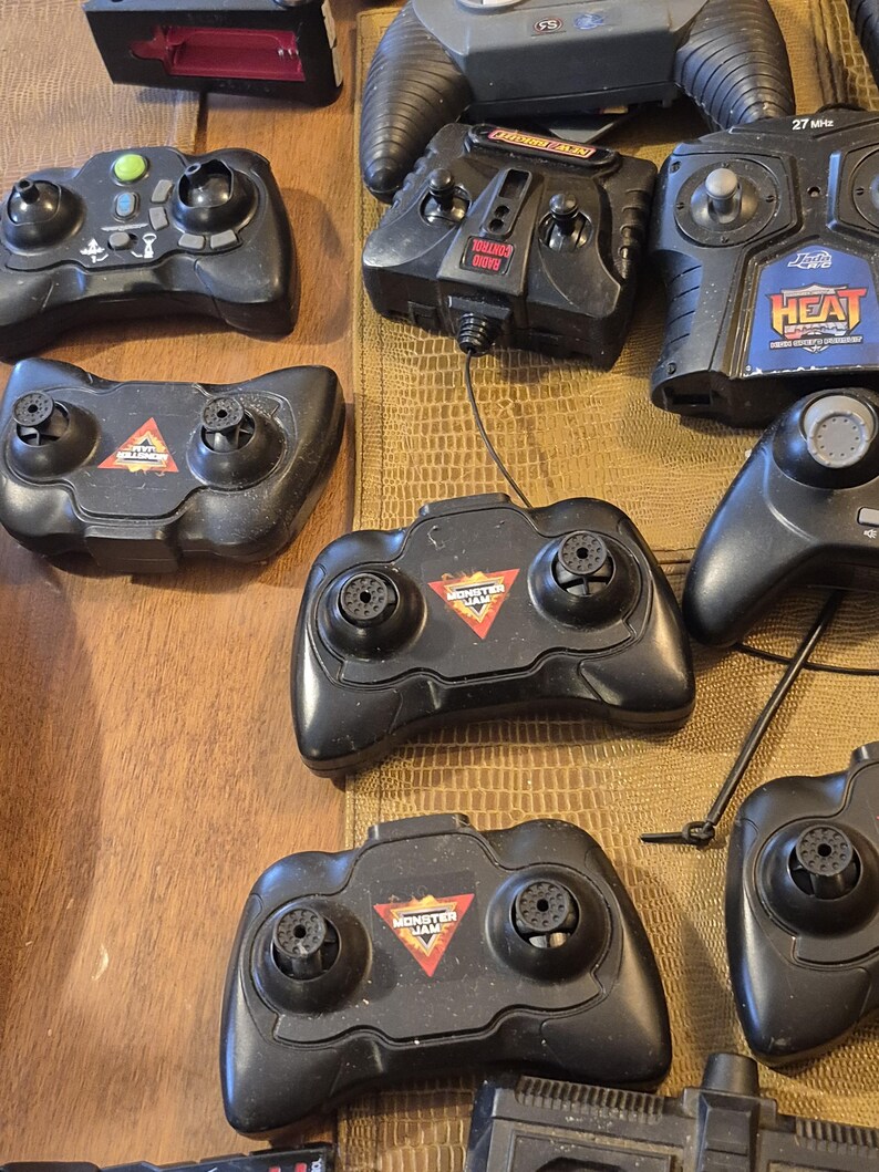 Pu&ograve; includere: Una collezione di telecomandi neri, alcuni con il logo "Monster Jam". I telecomandi hanno vari layout di pulsanti e design, alcuni con antenne e altri con il logo "Heat".