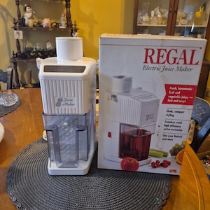 May include: A white ceramic mug with a black handle and the text "But First, Coffee" in a bold, black font. The mug is set against a blurred background, highlighting its clean design.