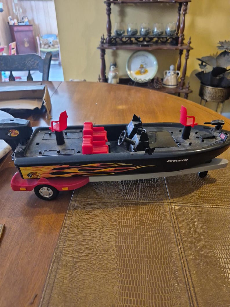 Puede incluir: Barco de pesca de juguete negro y rojo con un remolque. El barco tiene un dise&ntilde;o de llama roja y amarilla y el texto "670 ION" en el lateral. El barco tiene asientos rojos y un volante.