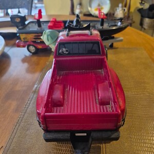 Puede incluir: Una camioneta de juguete roja con una caja negra y un enganche negro. La camioneta tiene un portaequipajes de techo negro y una pegatina en la parte trasera que dice "Bass Pro Shops".