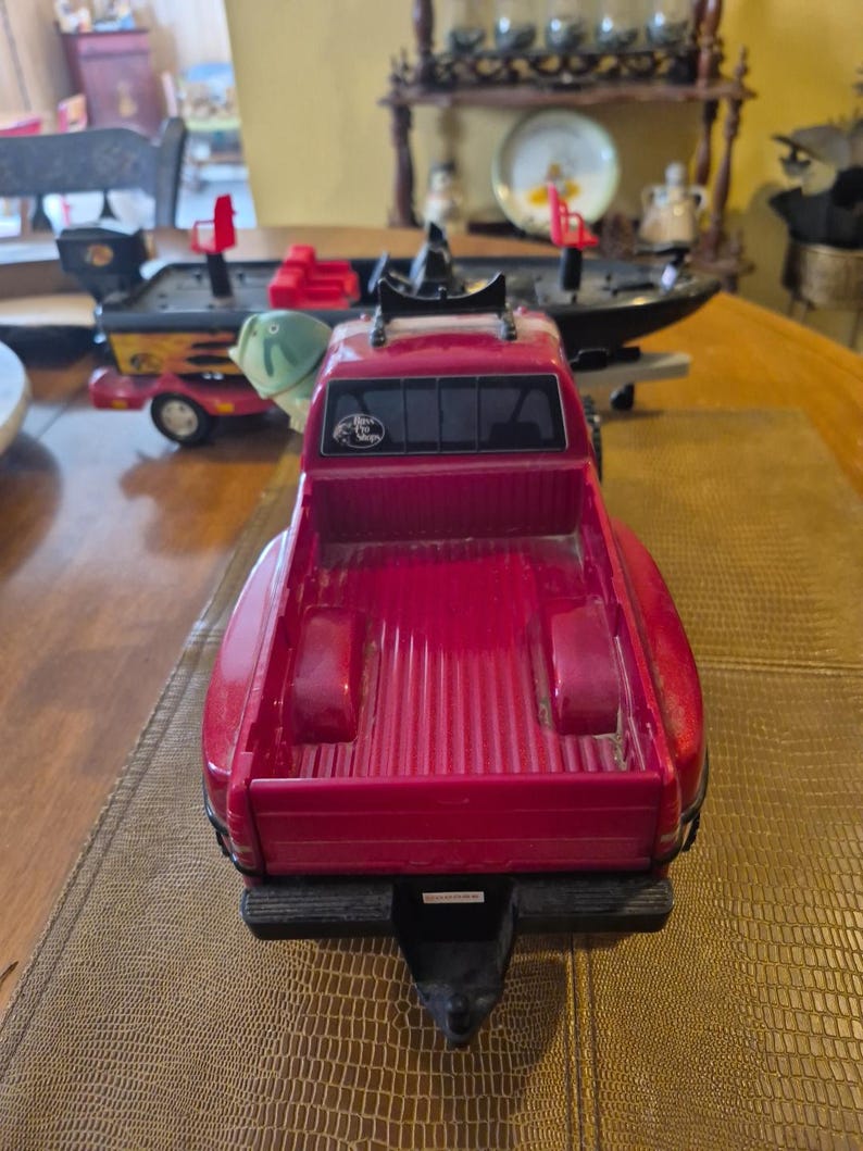 Puede incluir: Una camioneta de juguete roja con una caja negra y un enganche negro. La camioneta tiene un portaequipajes de techo negro y una pegatina en la parte trasera que dice "Bass Pro Shops".