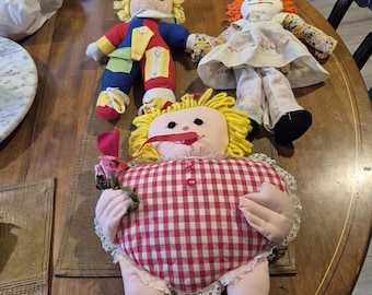 Three vintage dolls. The first is j s n y learn to dress doll clown. The second is raggedy and knickerbocker doll. The third is ginghsm