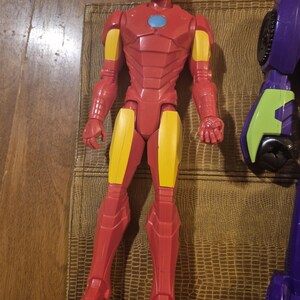 May include: A plastic Iron Man action figure featuring a red and yellow suit with a light blue circular chest piece. The figure stands in an upright position with articulated limbs, a detailed helmet, and molded armor plating across the torso and legs.