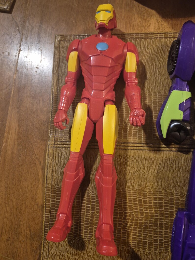May include: A plastic Iron Man action figure featuring a red and yellow suit with a light blue circular chest piece. The figure stands in an upright position with articulated limbs, a detailed helmet, and molded armor plating across the torso and legs.